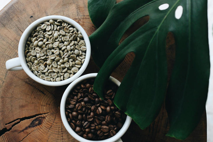 Grains de café verts et torréfiés dans deux tasses avec une feuille verte.