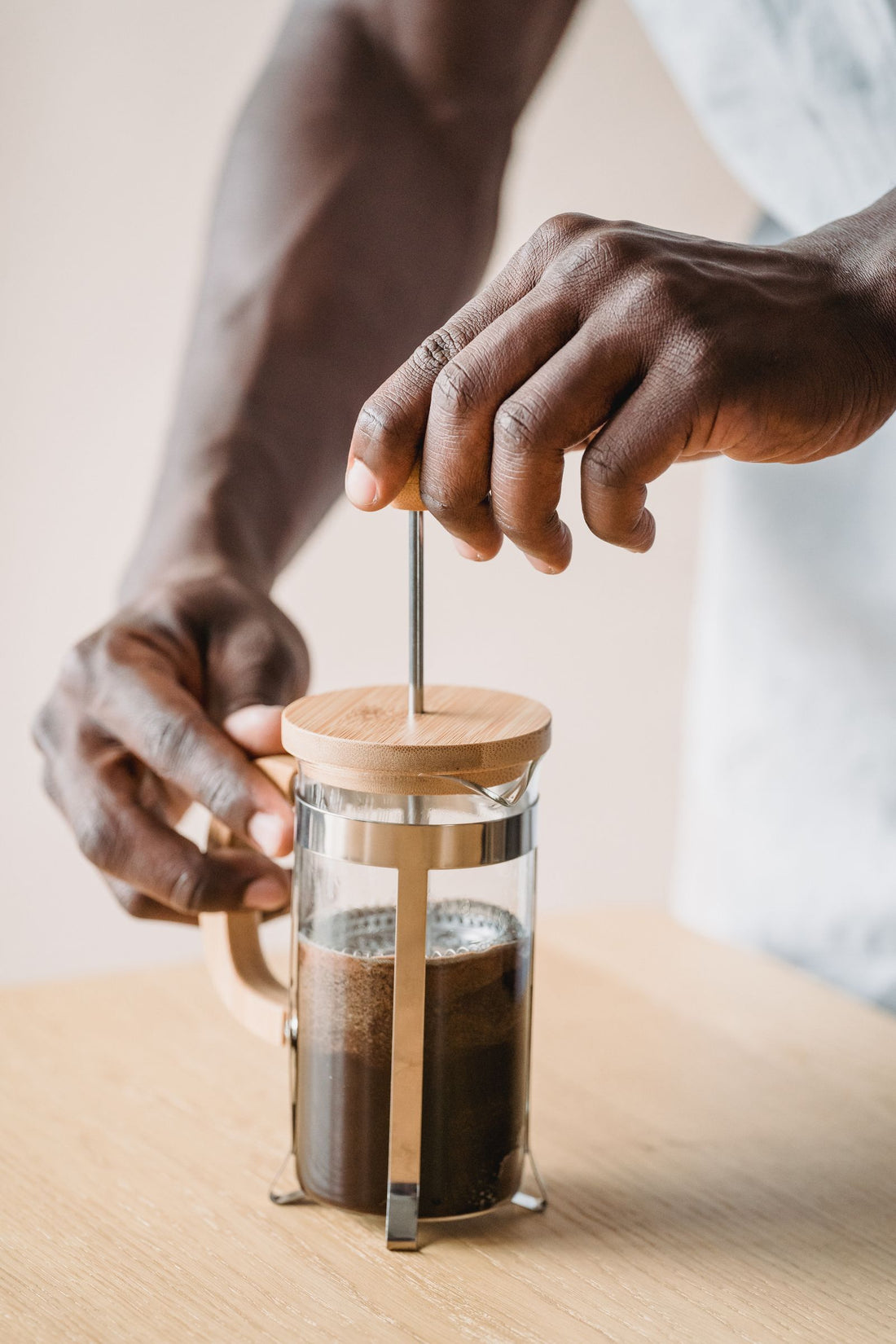 Personne utilisant une French press pour préparer du café sur une table en bois.