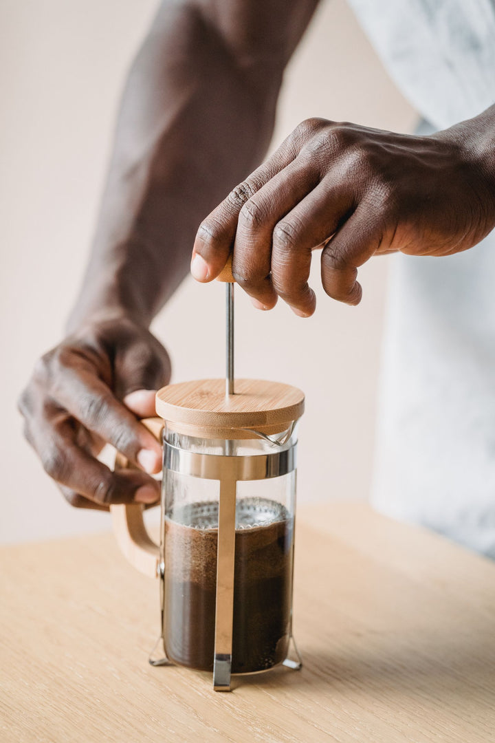 Personne utilisant une French press pour préparer du café sur une table en bois.