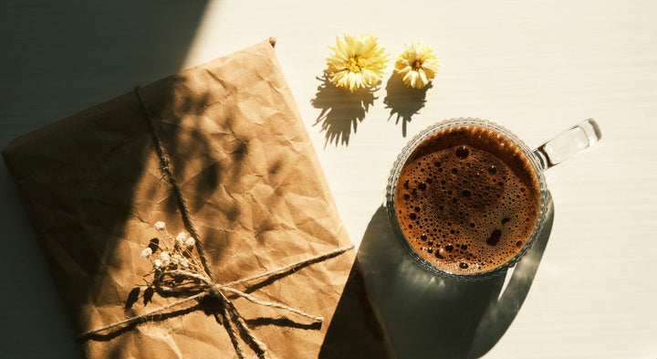 Tasse de café et paquet cadeau en papier kraft sur une table ensoleillée.