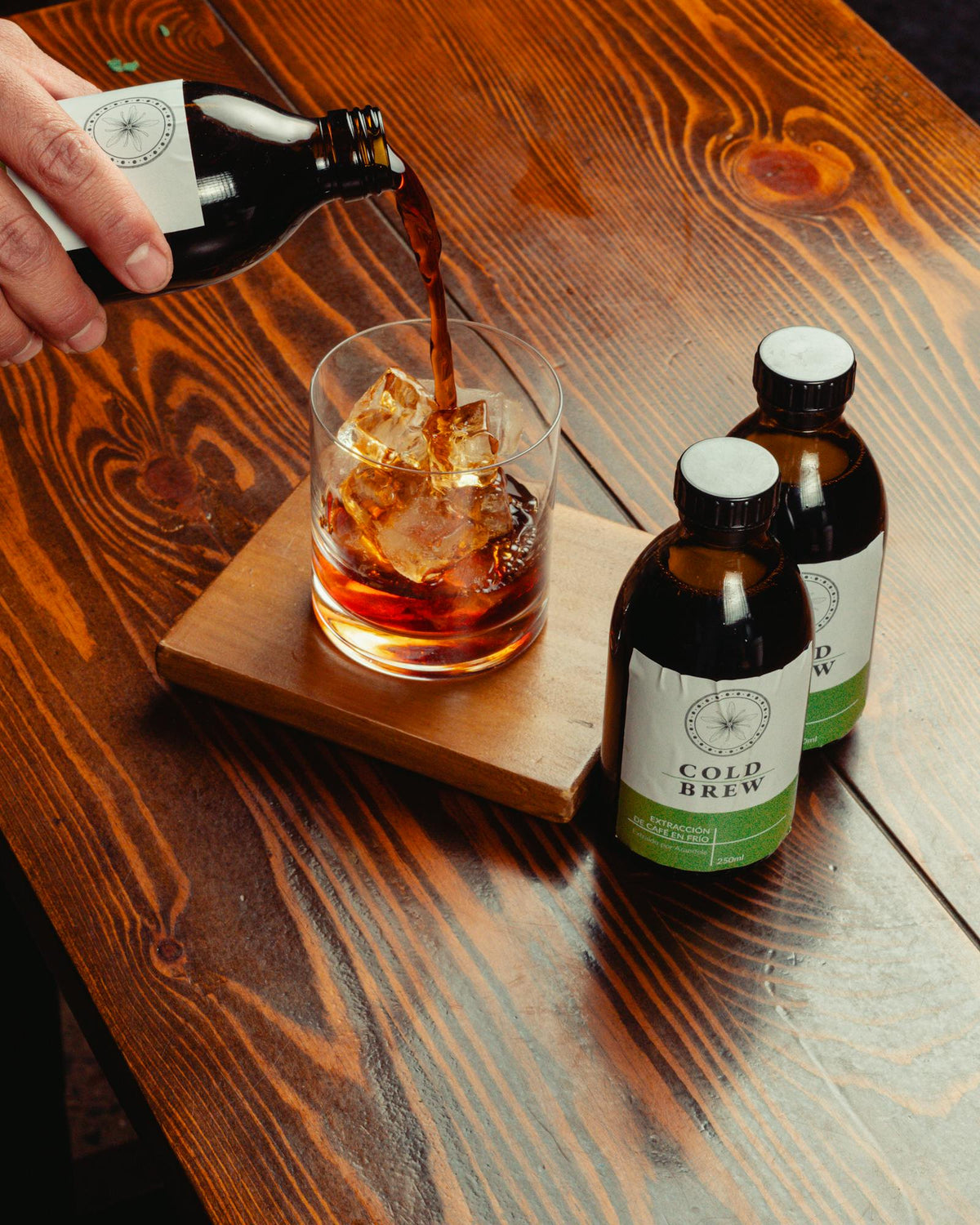 Cold brew versé sur des glaçons dans un verre posé sur une table en bois.