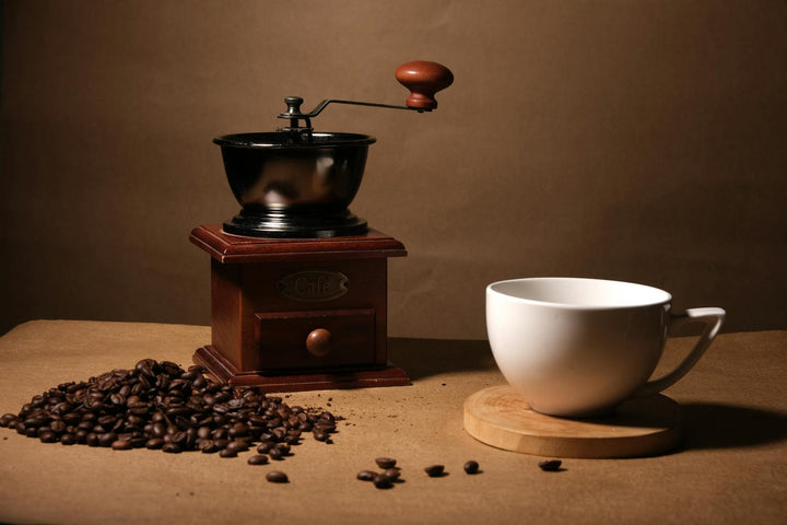 Moulin à café vintage, grains de café et tasse blanche dans une lumière chaude.