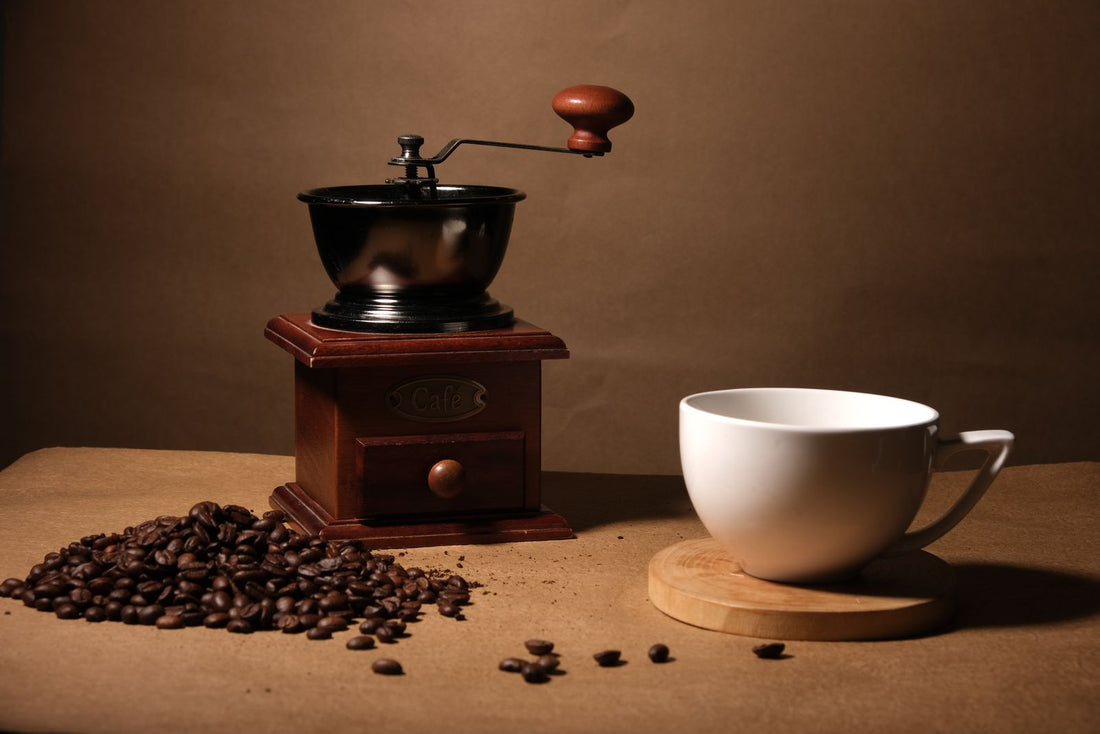 Moulin à café ancien, grains éparpillés et petite tasse dans une lumière chaude du matin.