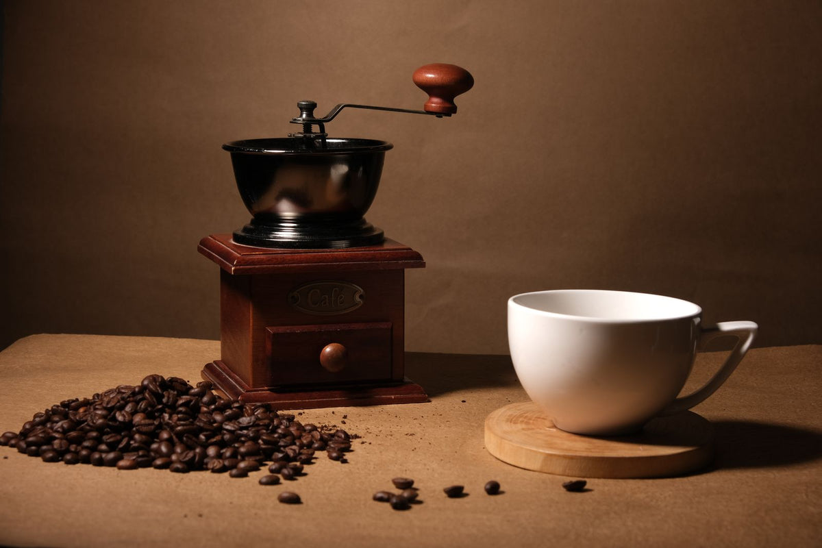 Moulin à café ancien, grains éparpillés et petite tasse dans une lumière chaude du matin.