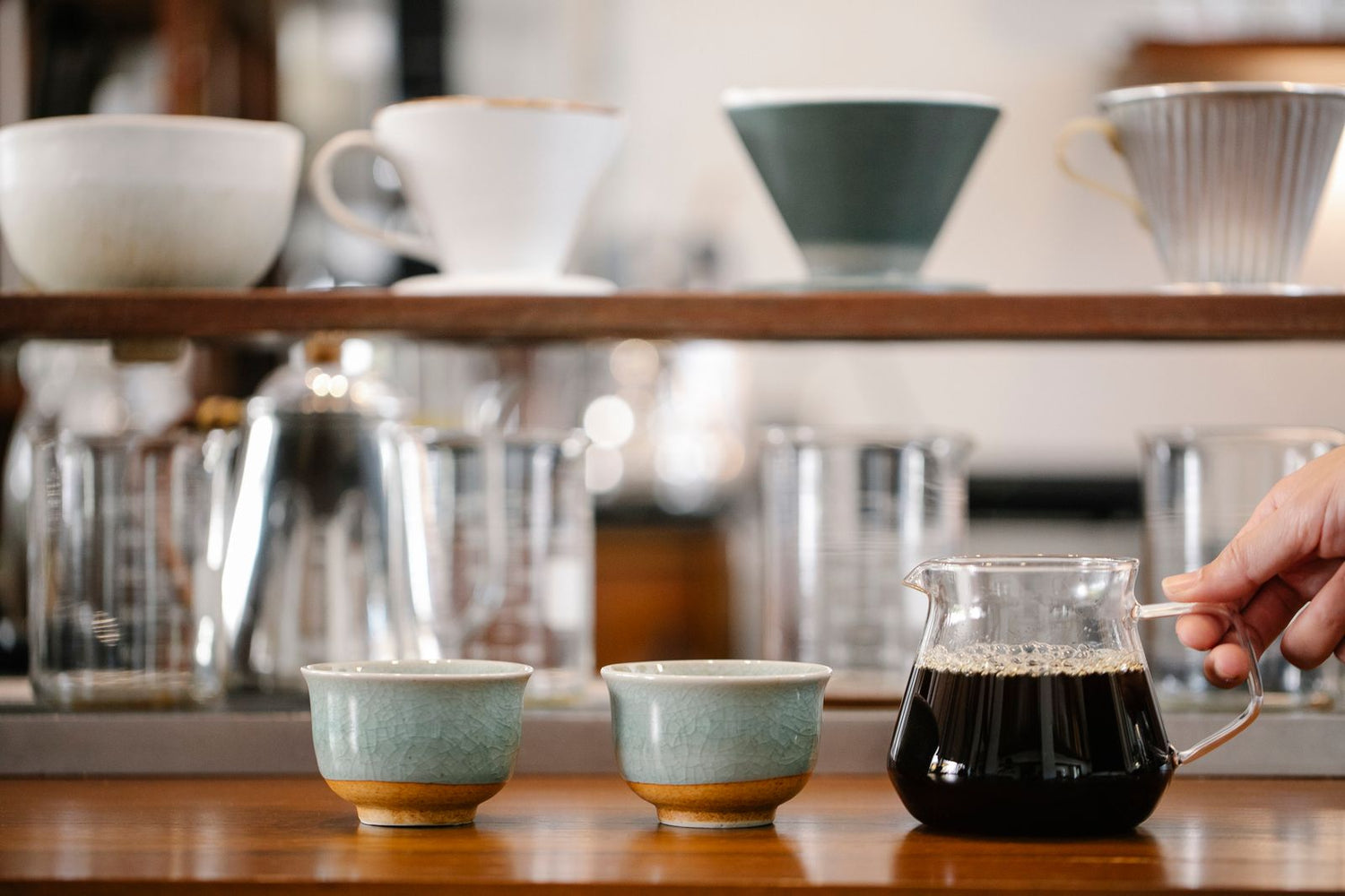 Une table de dégustation de café avec une carafe en verre et plusieurs tasses blanches alignées, prêtes pour la comparaison.
